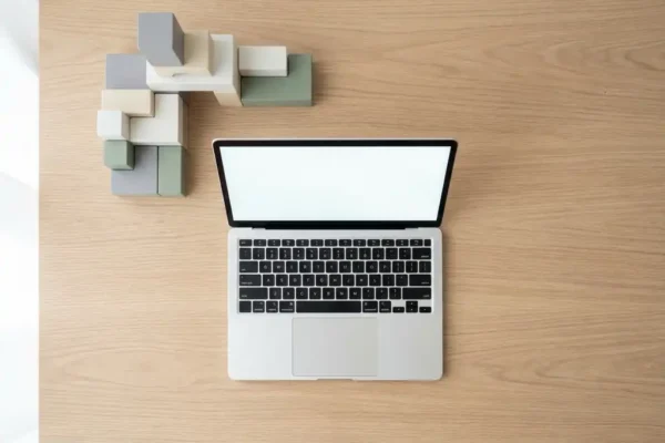 Houten bureau met open laptop en geometrische bouwblokken in grijs en wit, bovenaanzicht in zacht natuurlijk licht.
